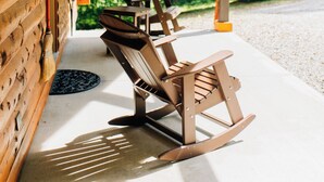 Une cabane en bois dotée d’un porche, de chaises berçantes et d’un banc en bois.