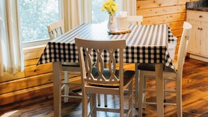 L’intérieur d’un chalet en bois, avec une table à manger dressée pour quatre personnes, un luminaire suspendu et une fenêtre avec des rideaux.