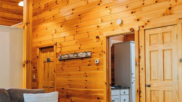 Un intérieur en bois avec un canapé, une table blanche et un coin cuisine visible à travers une porte ouverte.