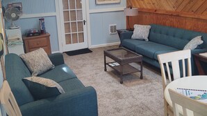 A living room with a blue sofa, a coffee table, and a TV mounted on the wall. - Ocean Beach, Fire Island,NY 4 bed,2 Bath, Sleeps 9, Full Kitchen, Deck, Bicycles (Ocean Beach)
