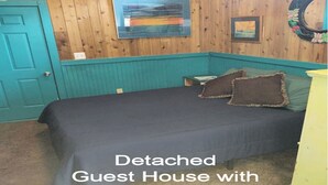 A detached guest house with a private bath, featuring a wooden interior, a bed with dark bedding, and a teal accent wall. - Ocean Beach, Fire Island,NY 4 bed,2 Bath, Sleeps 9, Full Kitchen, Deck, Bicycles (Ocean Beach)
