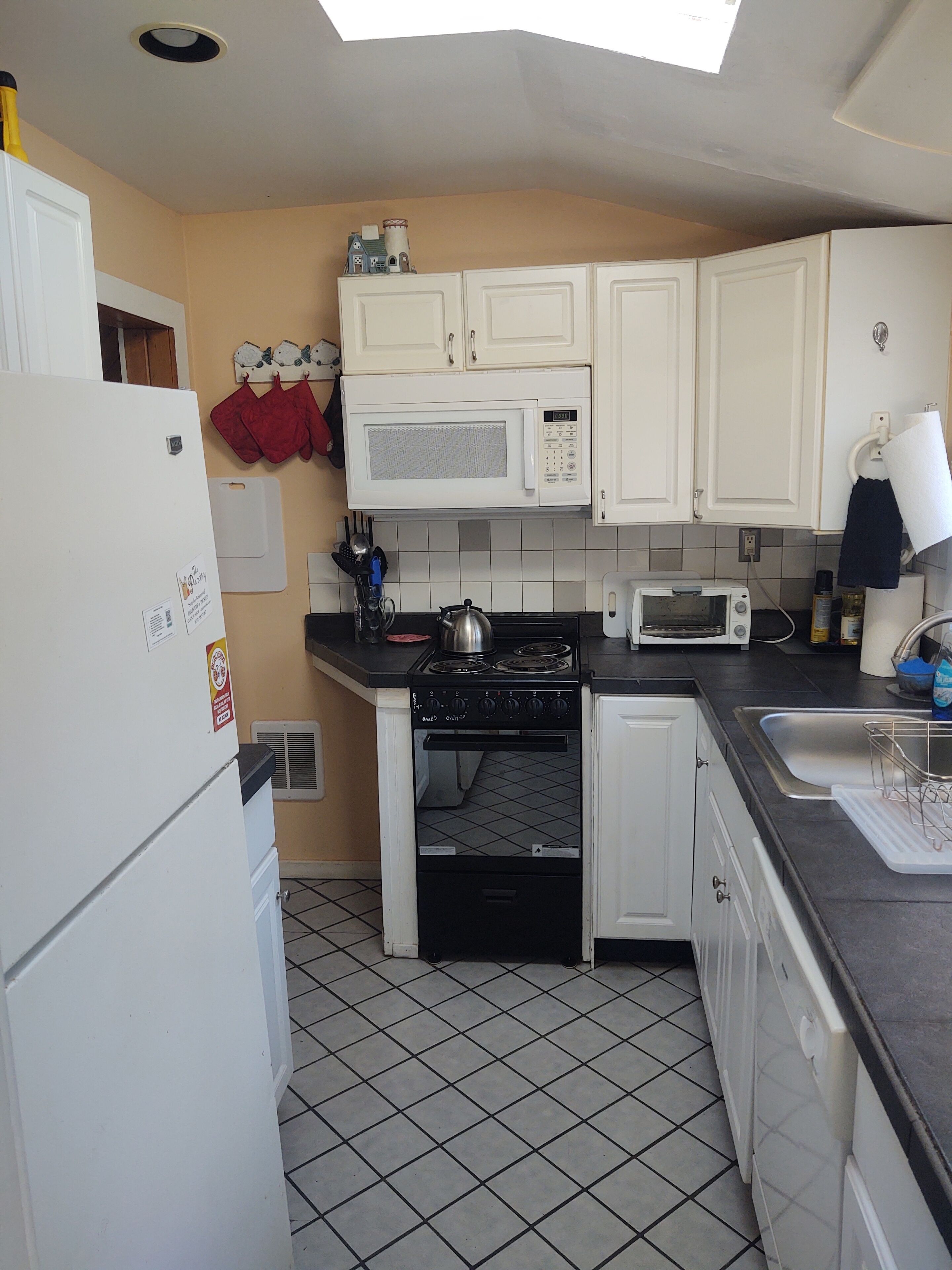 A compact kitchen with white cabinets, a microwave, a stove, and a toaster.