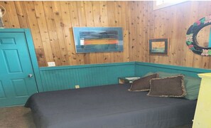 A detached guest house with a private bath, featuring a wooden interior, a bed with dark bedding, and a teal accent wall. - Ocean Beach, Fire Island,NY 4 bed,2 Bath, Sleeps 9, Full Kitchen, Deck, Bicycles (Ocean Beach)