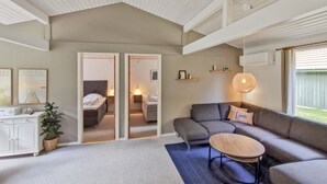 Una sala de estar moderna con un sofá gris, una mesita redonda y un ventanal con vistas al exterior.