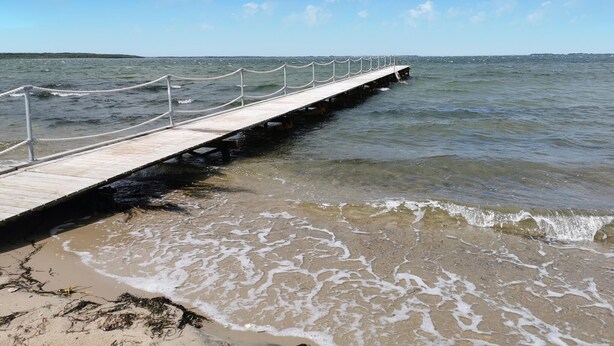 Un muelle de madera que se adentra en aguas tranquilas bajo un cielo despejado.