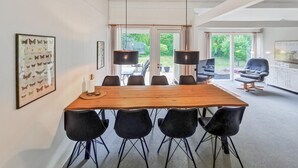 Un comedor con una mesa de madera y sillas negras, una obra de arte con mariposas enmarcadas en la pared y vistas al jardín a través de grandes ventanales.