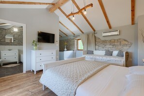 A bedroom with a bed, a dresser, a TV, and a stone wall.