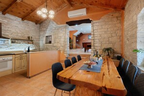 A rustic interior with a long wooden dining table, stone walls, and a piano in the background.