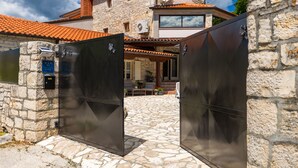 A stone building with a tiled roof, a covered patio, and a large metal gate. - Villa Antoli (Istria - Jakovici) (Jakovici)
