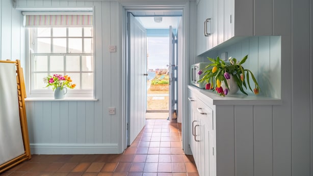 A narrow hallway with a window on the left, a door at the end, and a kitchen area on the right.
