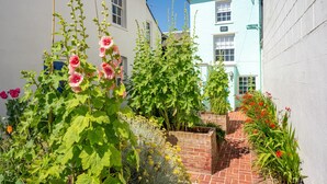 A narrow brick pathway leading to a row of houses with a garden in the foreground.