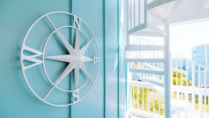 Una habitación con una escalera espiral blanca, barandilla blanca y una gran decoración de brújula en la pared.