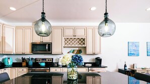Una cocina con armarios de madera, una isla central, un microondas y lámparas colgantes.