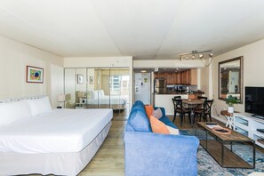A hotel room with a bed, a sofa, a dining table with chairs, a kitchen area, and a TV.