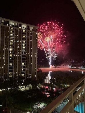 A high-rise building with multiple balconies and a view of a fireworks display in the distance.