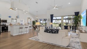 A spacious living area with a white sofa, a dining table, and a kitchen area with white cabinets and a microwave. - Golf Course View, Putting Green, Heated Pool and Spa - Villa Fairway to Heaven - Roelens (Cape Coral)