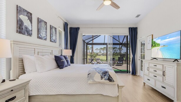 A bedroom with a bed, a TV, a ceiling fan, and a view of the outdoors. - Golf Course View, Putting Green, Heated Pool and Spa - Villa Fairway to Heaven - Roelens (Cape Coral)