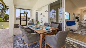 A dining area with a wooden table, wicker chairs, and a view of the outside. - Golf Course View, Putting Green, Heated Pool and Spa - Villa Fairway to Heaven - Roelens (Cape Coral)