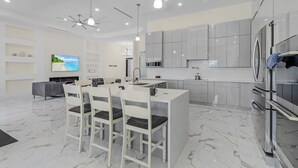 Una cucina moderna con mobili grigi, un'isola centrale con sedute, un televisore e una ventola a soffitto.