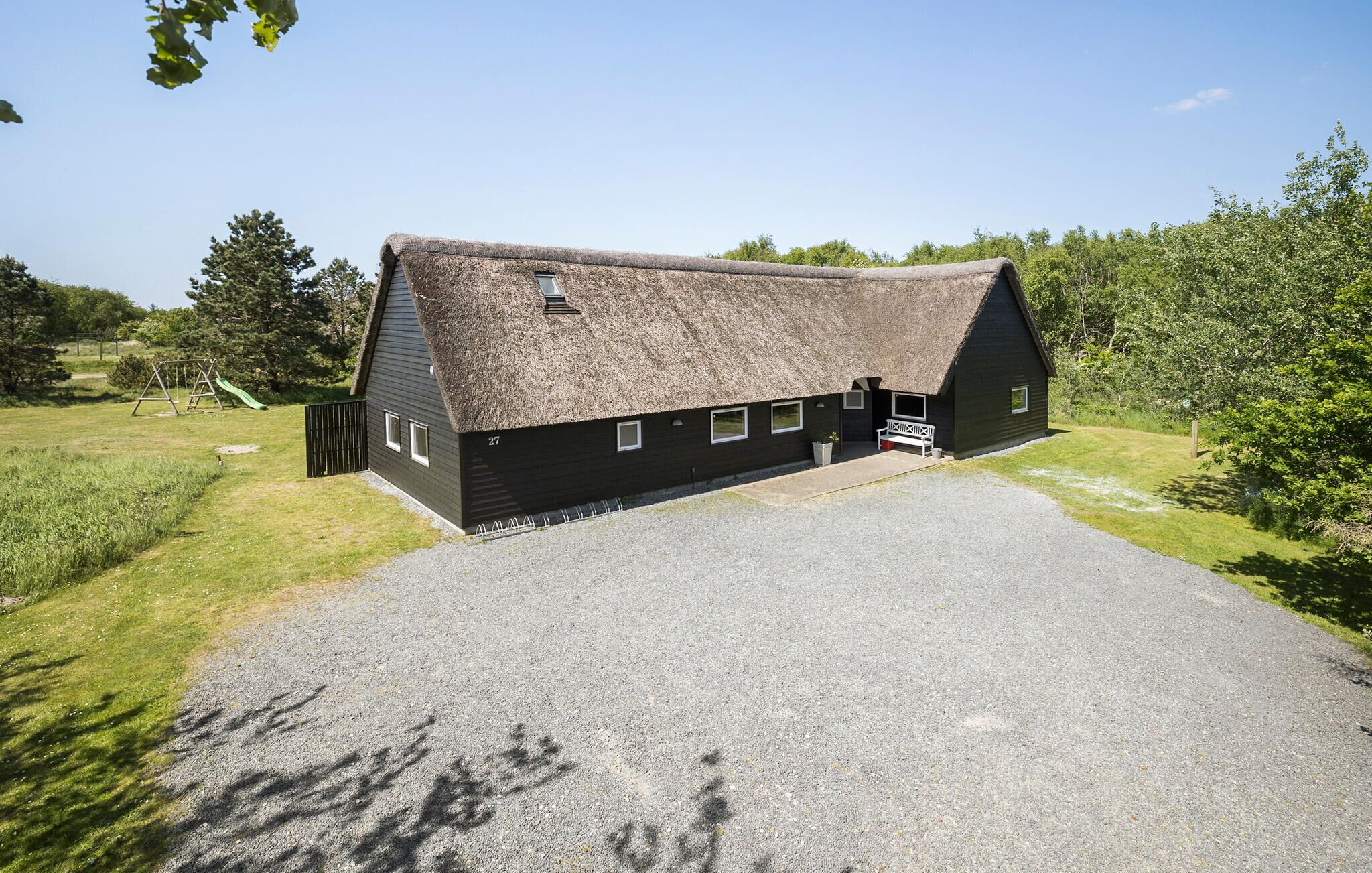 A black building with a thatched roof, a gravel driveway, and a small porch.
