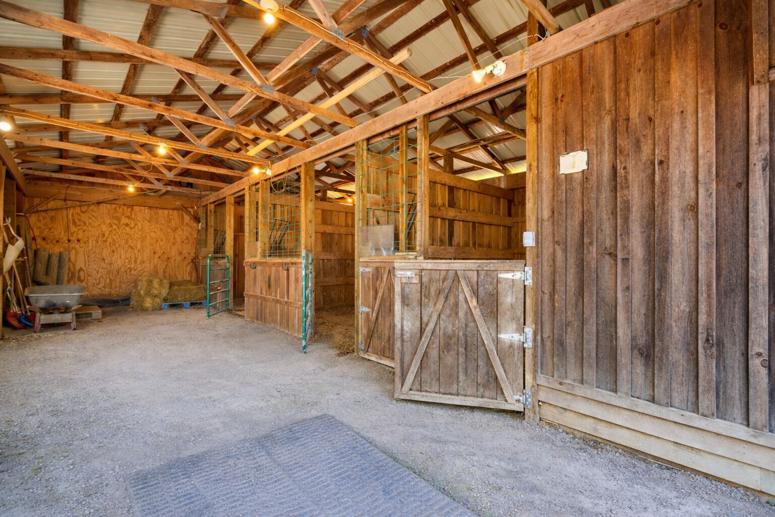 A barn interior with wooden walls, a metal door, hay bales, and a concrete floor.