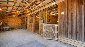A barn interior with wooden walls, a metal door, hay bales, and a concrete floor.