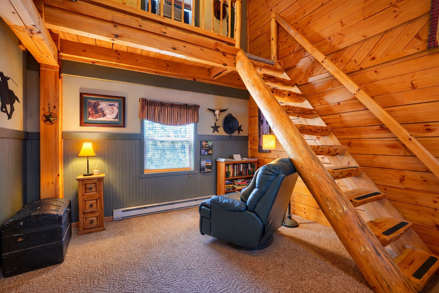 A cozy room with a sloped ceiling, a wooden staircase, a comfortable chair, a small table with a lamp, and a bookshelf.