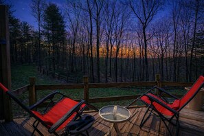 Una terraza con dos sillas rojas y una mesa, con vistas a un área boscosa al atardecer.