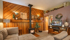 A cozy living room with a fireplace, comfortable seating, a television, and decorative items. - Carp's Cabin: 2 Bedroom Farmhouse Bungalow (Logan)