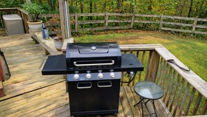Ein Grill auf einer Holzterrasse mit einem Metalltisch und einem Stuhl in der Nähe.