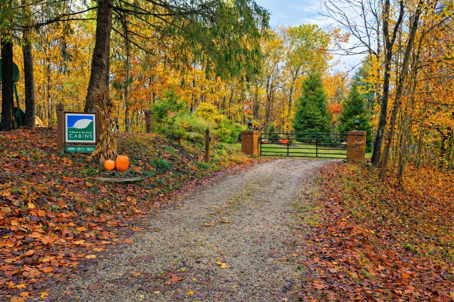 A gravel path leading to a gated entrance with autumn foliage and a sign for 'A Retreat in the Rural Cabins.'