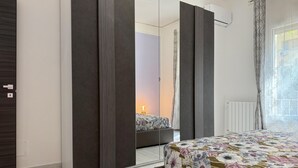 A bedroom with a large mirror, a bed with a floral bedspread, a bedside table with a lamp, and a window with curtains. - 3 bedroom amazing apartment in Palermo (Palermo)
