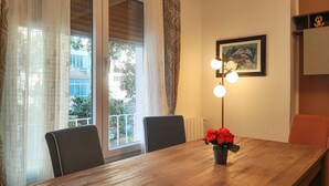 A dining area with a wooden table, two chairs, a vase with red flowers, a floor lamp, and a framed picture on the wall. - 3 bedroom amazing apartment in Palermo (Palermo)