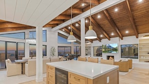 A spacious kitchen with a large island, wooden beams, and large windows offering views of the outdoors.