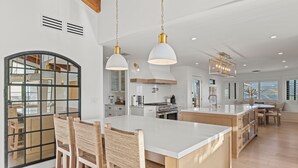 A spacious kitchen with a large island, wooden chairs, and pendant lighting.