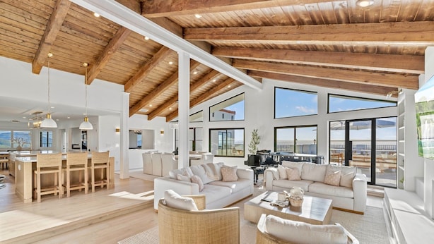A spacious living area with a high ceiling, large windows, and a modern kitchen in the background.