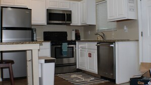 Una cocina con armarios blancos, electrodomésticos de acero inoxidable, microondas, horno y lavavajillas.