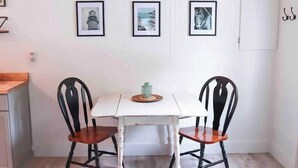 A dining area with a white table and two black chairs with wooden seats. There are three framed pictures on the wall above the table. - MaineStay Cottage #2 Bangor/Hampden close to town (Hampden)