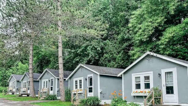 A row of small, single-story cabins with white trim and grey exteriors, set in a wooded area with a gravel path leading to them. - MaineStay Cottage #2 Bangor/Hampden close to town (Hampden)