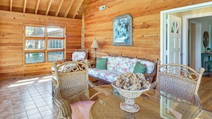 A wooden cabin interior with a sofa, wicker chairs, a glass table, and a window with four panes. - Lakefront Leesburg Home w/ Private Dock & Ramp! (Leesburg)