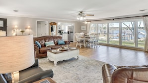 A spacious living room with a large window, a ceiling fan, and a dining area with a view. - Lakefront Leesburg Home w/ Private Dock & Ramp! (Leesburg)