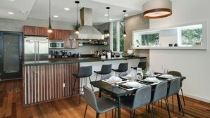 Une cuisine moderne dotée d’un îlot central, d’appareils électroménagers en acier inoxydable et d’un coin repas avec des chaises grises et une table dressée pour quatre personnes.