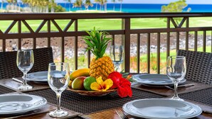 Una mesa de comedor dispuesta con platos, vasos y una cesta de frutas con piña, mango e hibisco.