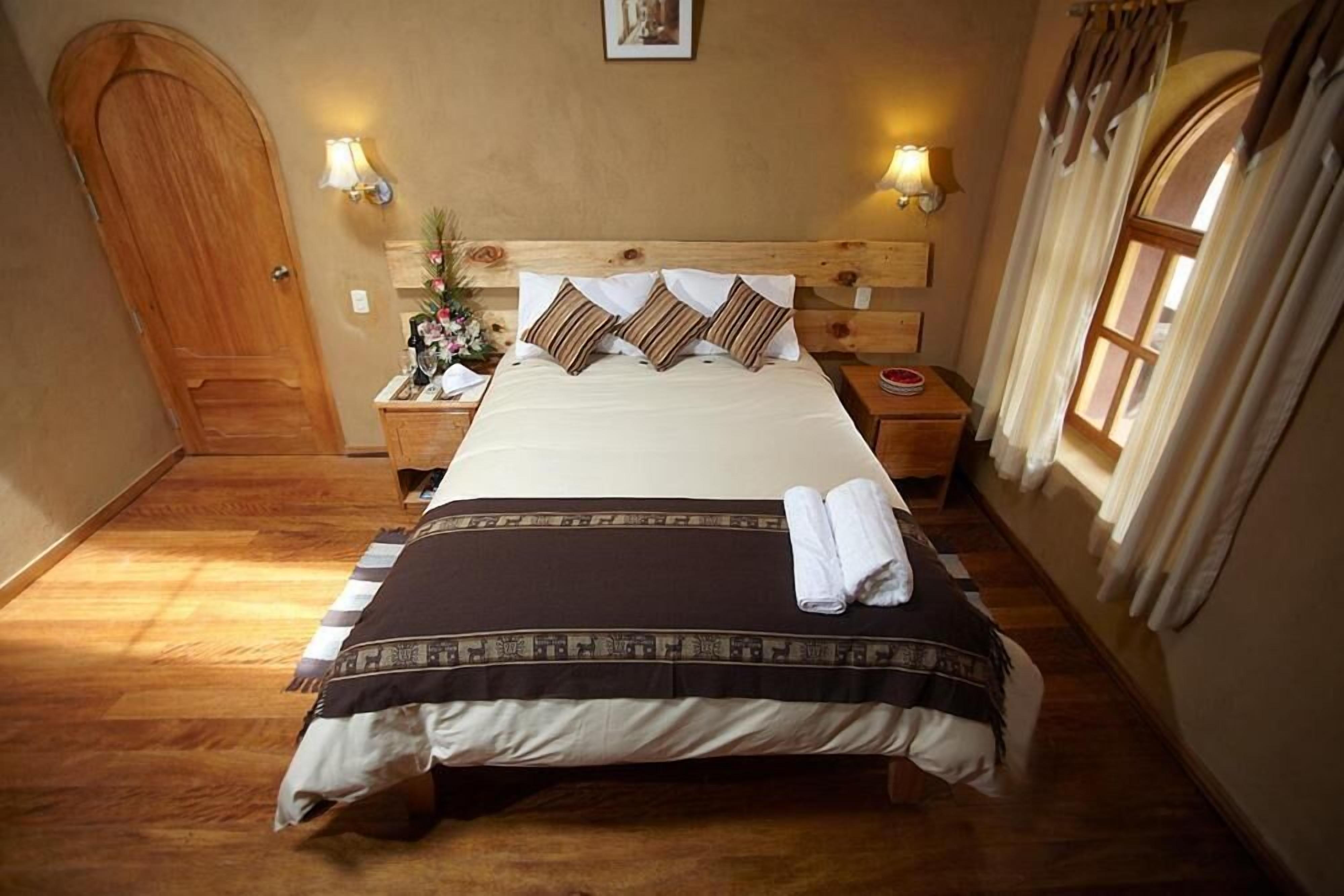 Une chambre à coucher bien rangée, avec une tête de lit en bois, un lit agrémenté d’oreillers à rayures, deux tables de chevet avec des lampes et une fenêtre avec des rideaux.