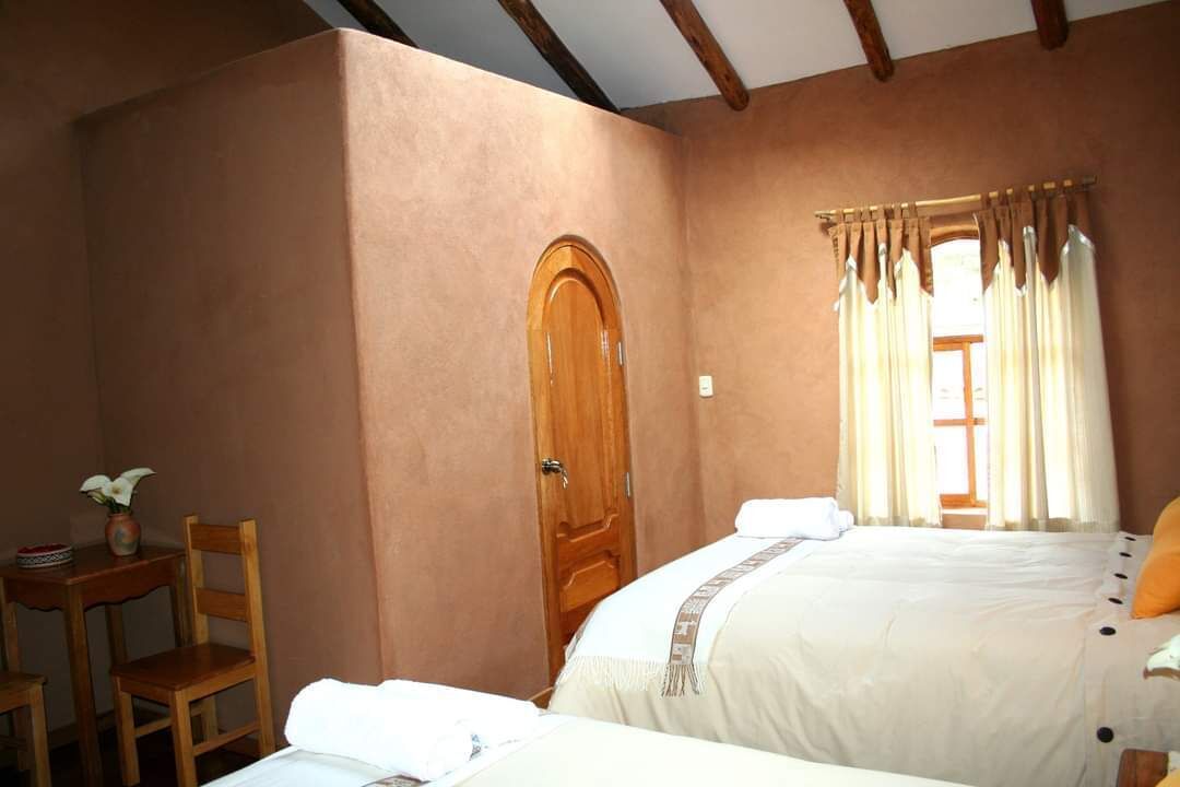 Een slaapkamer met een houten deur, een raam met gordijnen, een bed met wit beddengoed en een klein tafeltje met een stoel.