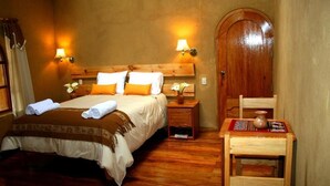 Une chambre d’hôtel avec un lit en bois, deux lampes de chevet, une table de chevet en bois, une petite table avec un vase et une porte en bois.