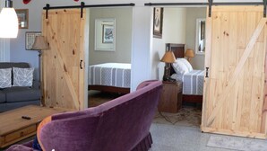 A room with a purple sofa, a wooden sliding door, a bed with a white and gray striped bedspread, and a lamp on a wooden nightstand. - Country setting near Custer, Wi-Fi, AC, pet friendly w/fee. No cleaning fee. (Custer)