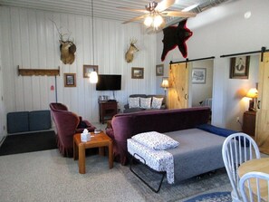 A room with a ceiling fan, mounted animal heads, a sofa, a chair, a small table, and a television.