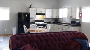 A living room with a dark red sofa, a dining table with chairs, and a kitchen area with white cabinets and appliances. - Country setting near Custer, Wi-Fi, AC, pet friendly w/fee. No cleaning fee. (Custer)