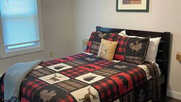 Une chambre à coucher avec un lit, un ventilateur de plafond, une fenêtre avec des stores et un tableau encadré au mur.